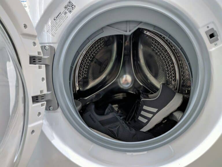 The washing machine's door is open, ready for action, with two black and white athletic shoes nestled inside the drum. As you prepare the washing machine, the shoes sit side by side, surrounded by the pristine interior waiting to unleash its cleaning magic.