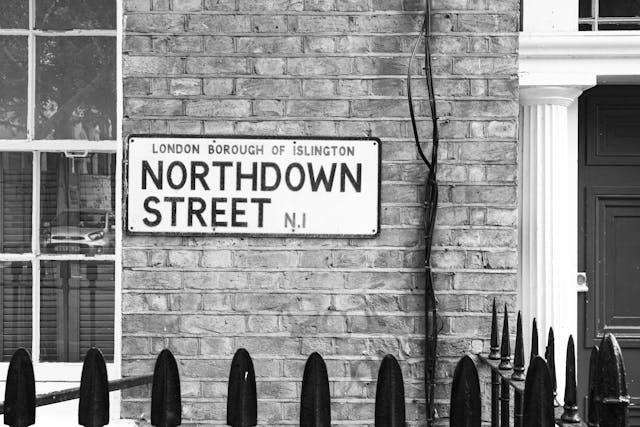 Black and white photo of a street sign reading "Northdown Street, London Borough of Islington, N1"—a glimpse into one of the hardest to move London boroughs—mounted on a brick wall by a white column, dark door, and iron railings in the foreground.