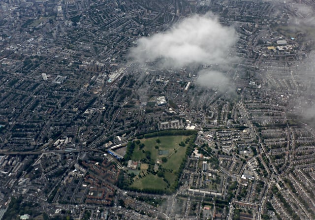 Aerial view of a dense urban area with a large green park at the centre, surrounded by buildings and roads—an inviting scene for anyone considering living in Hackney. A patch of white clouds partially obscures part of the city below, hinting at new perspectives and opportunities that come with moving to Hackney.