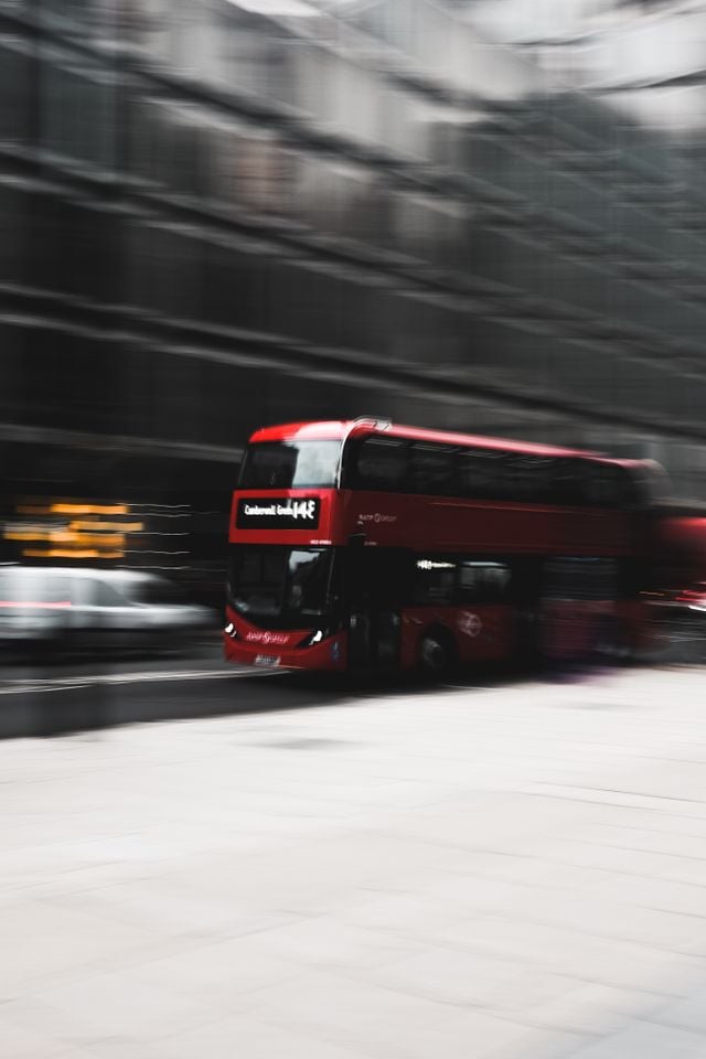 A red double-decker bus speeds through a city street in Islington, with surrounding buildings blurred, emphasising the motion and fast pace of urban life—capturing the vibrant energy you’ll experience when moving to Islington.