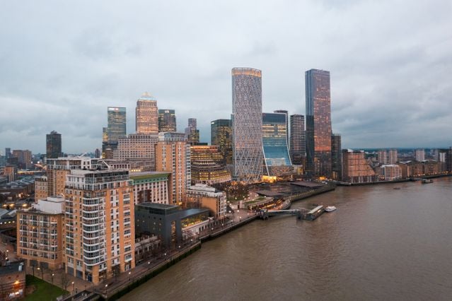 A cityscape of Canary Wharf in London, featuring modern skyscrapers and buildings along the River Thames under a cloudy sky at dusk—a striking view that captures the vibrant atmosphere for anyone considering moving to Canary Wharf.